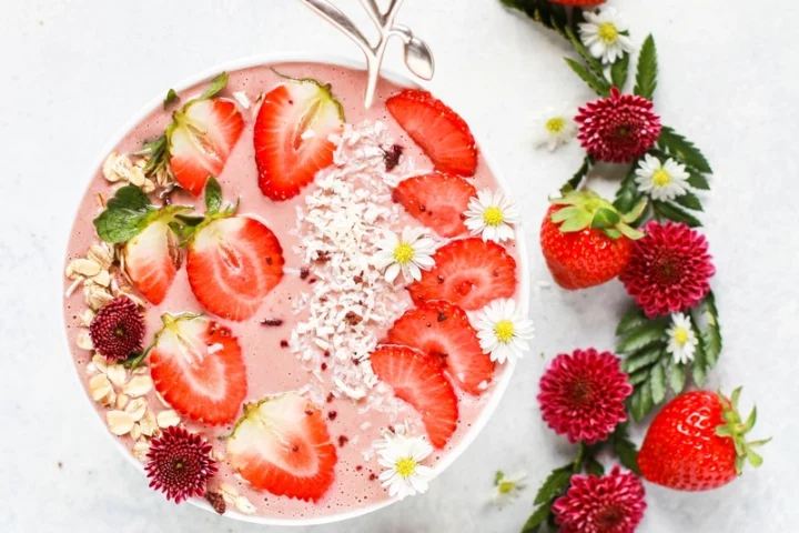 A pink strawberry smoothie bowl topped with sliced strawberries, oats and coconut