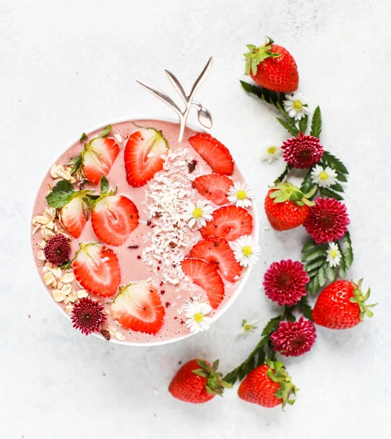 A pink strawberry smoothie bowl topped with sliced strawberries, oats and coconut
