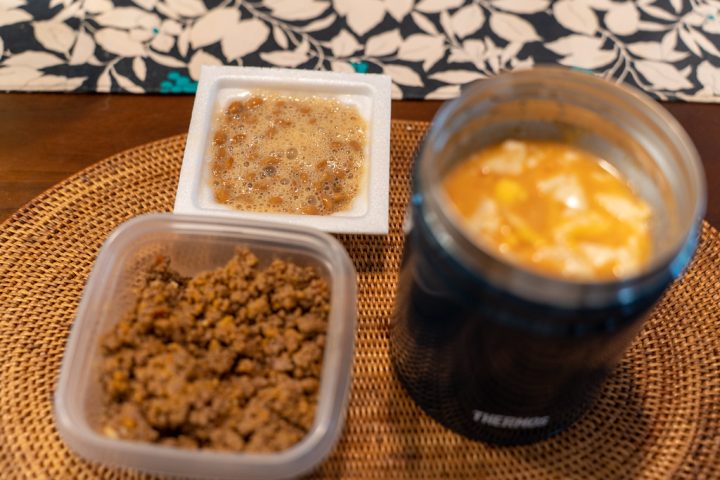 A packed lunch with an insulated food flask of soup beside two small containers of food