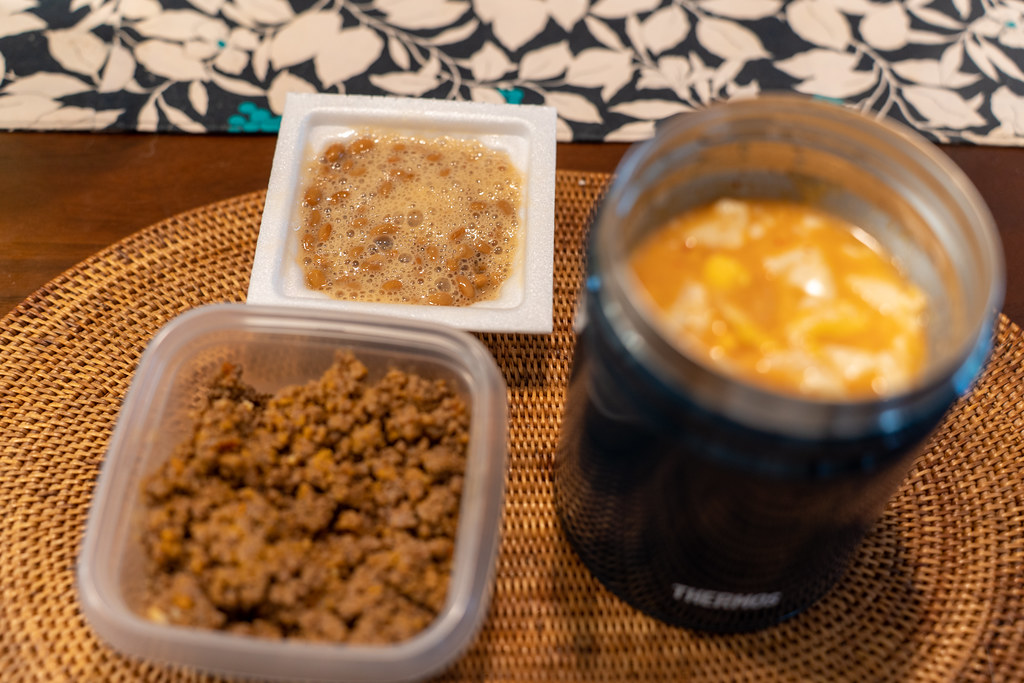 A packed lunch with an insulated food flask of soup beside two small containers of food