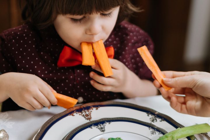 A small child eating carrot sticks from a plate at a dining table