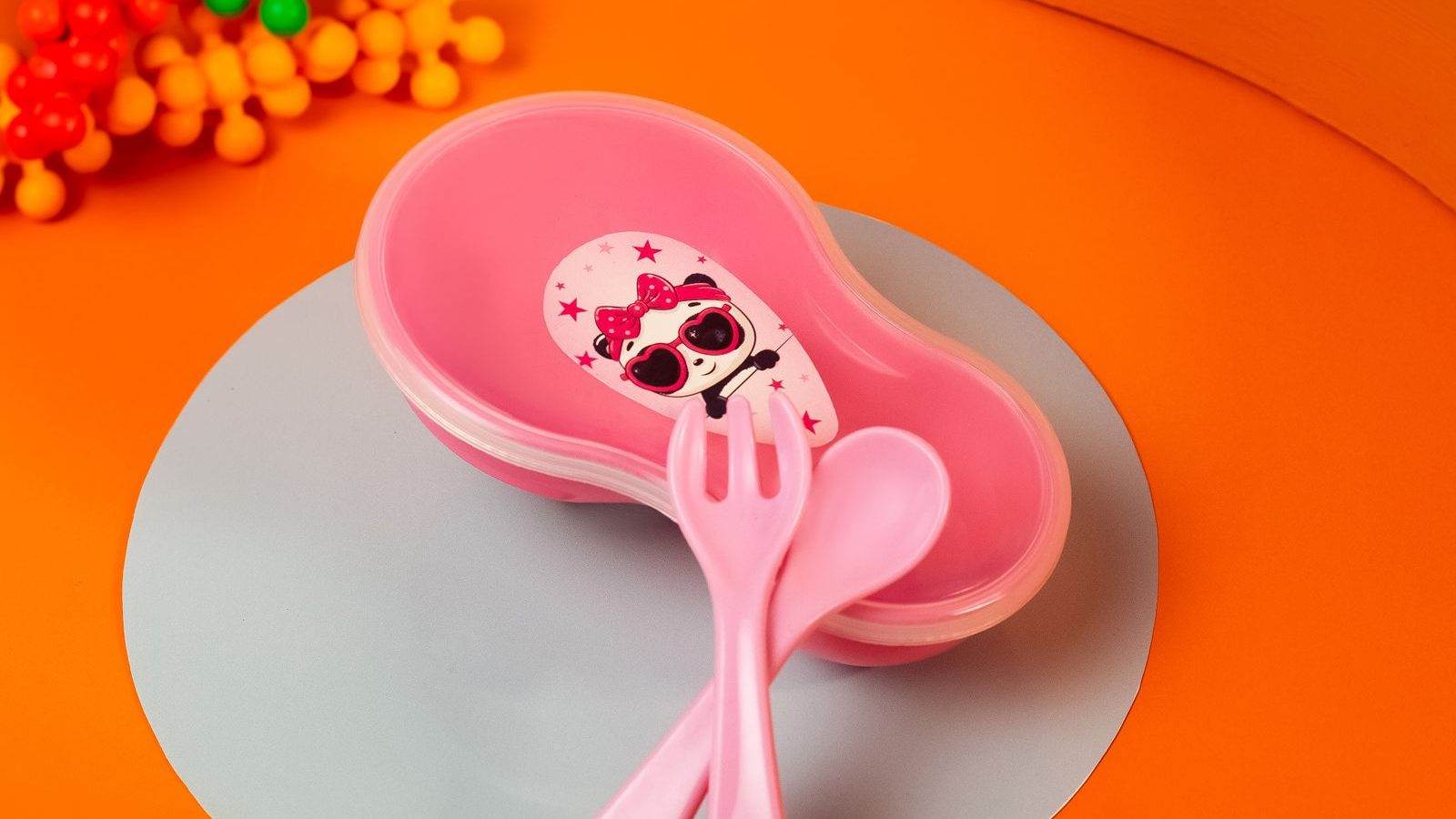 A pink toddler plate with a matching child-sized fork and spoon on an orange background
