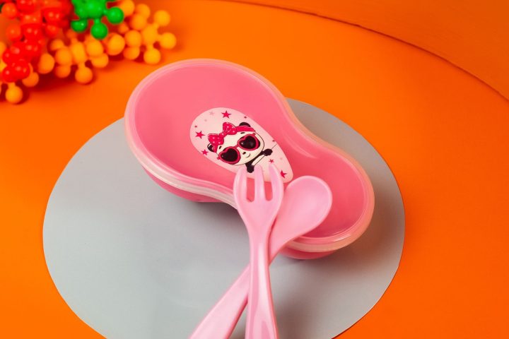 A pink toddler plate with a matching child-sized fork and spoon on an orange background