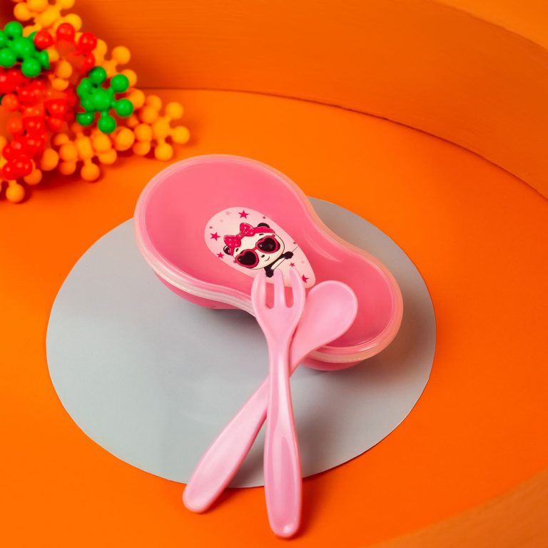 A pink toddler plate with a matching child-sized fork and spoon on an orange background