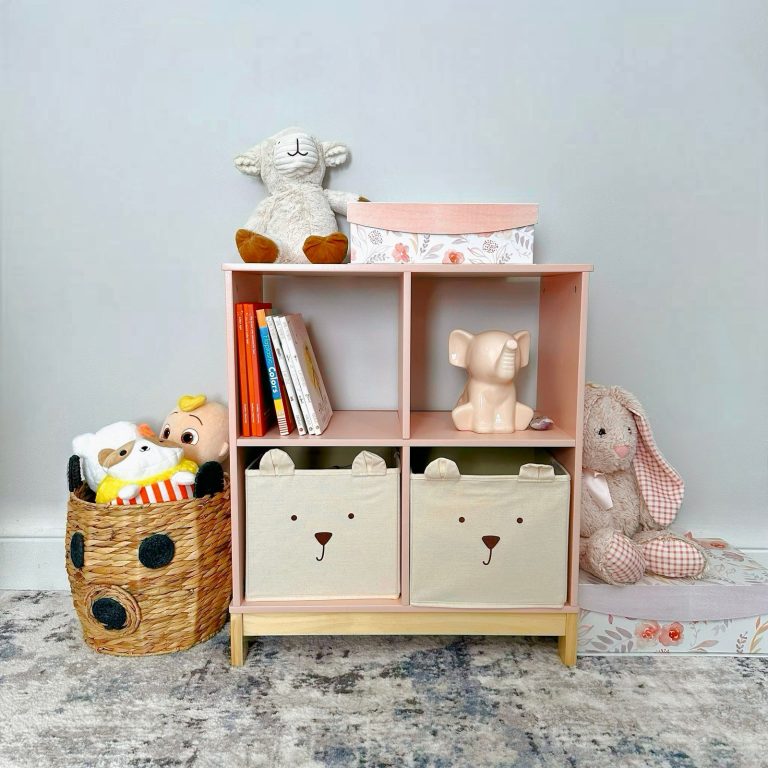 A cube shelf unit holding fabric storage bins, books and soft toys in a child room