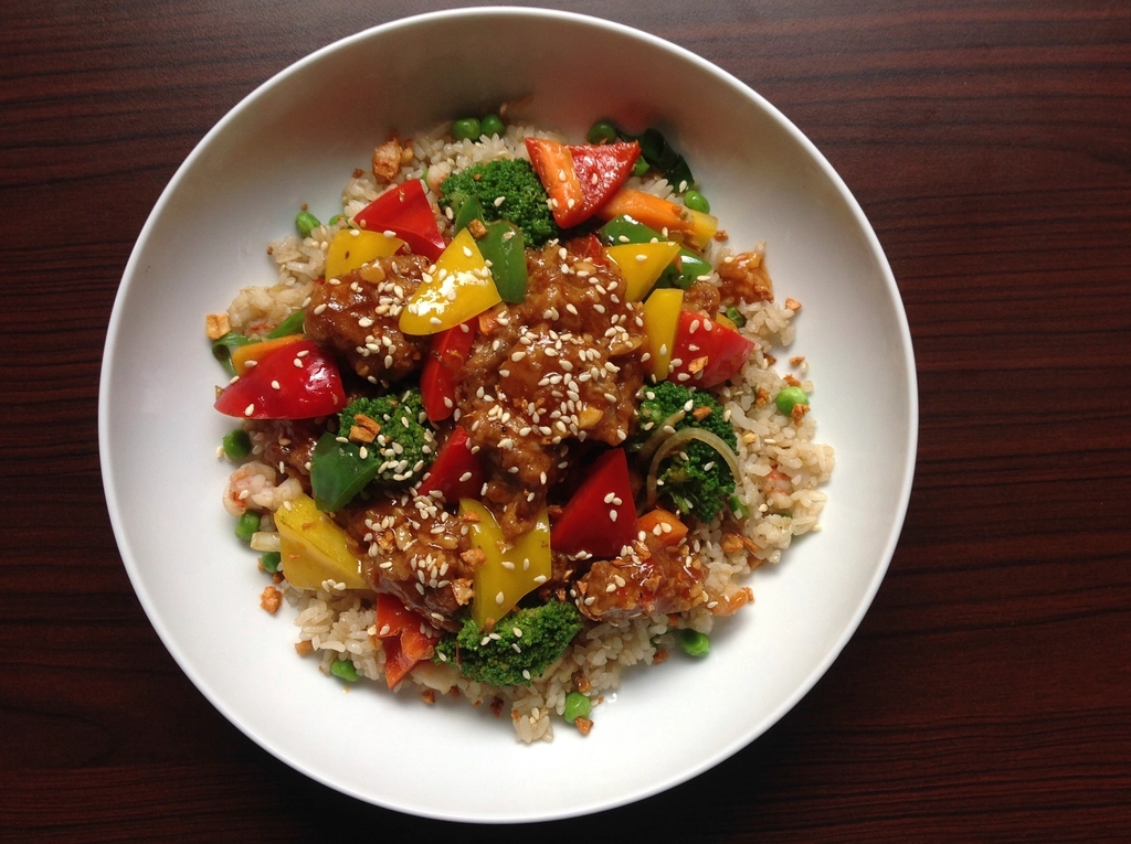 A bowl of rice mixed with chopped red and yellow peppers, tomato and herbs
