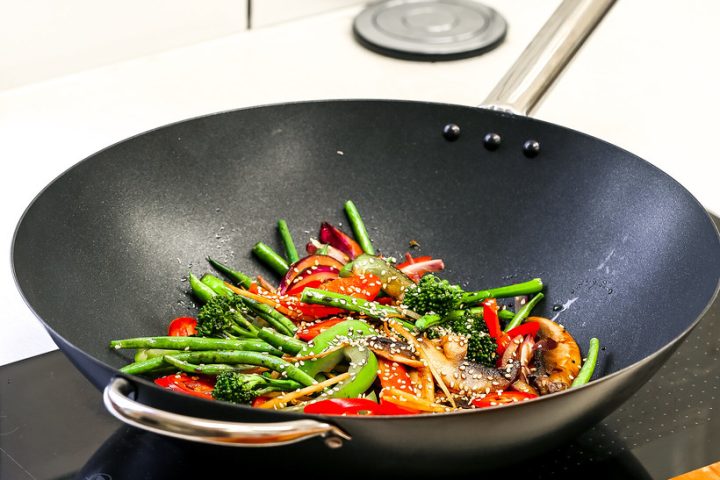 Mixed vegetables including broccoli, peppers and green beans cooking in a black wok