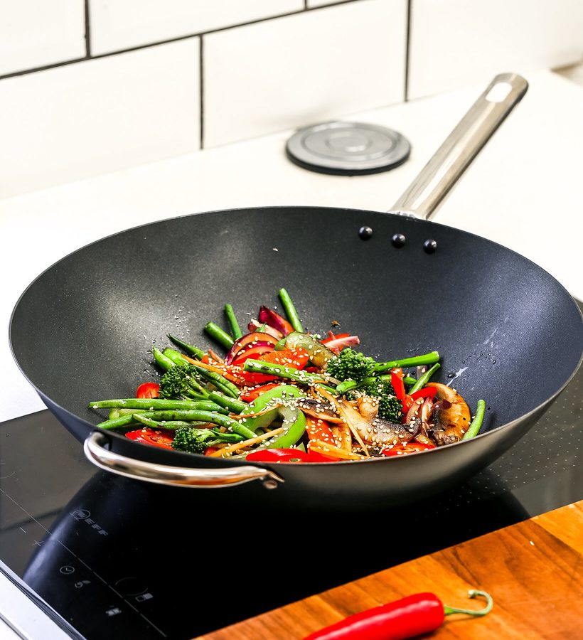 Mixed vegetables including broccoli, peppers and green beans cooking in a black wok