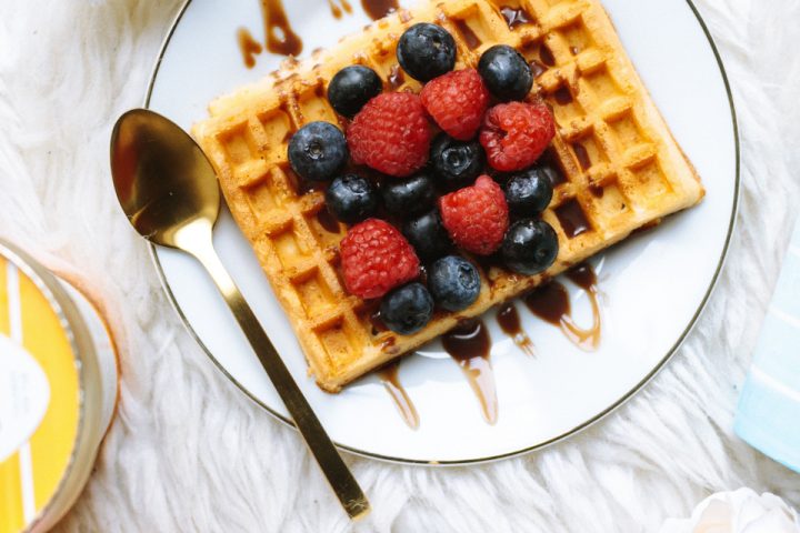 A waffle topped with fresh berries, served on a plate with a pot of cream