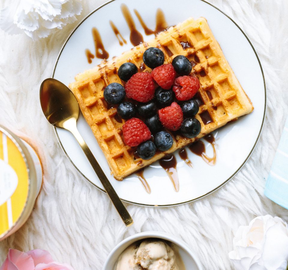 A waffle topped with fresh berries, served on a plate with a pot of cream