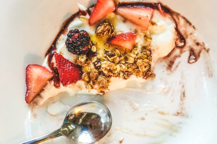 Yoghurt topped with sliced strawberries, berries and granola, with a spoon resting in the bowl