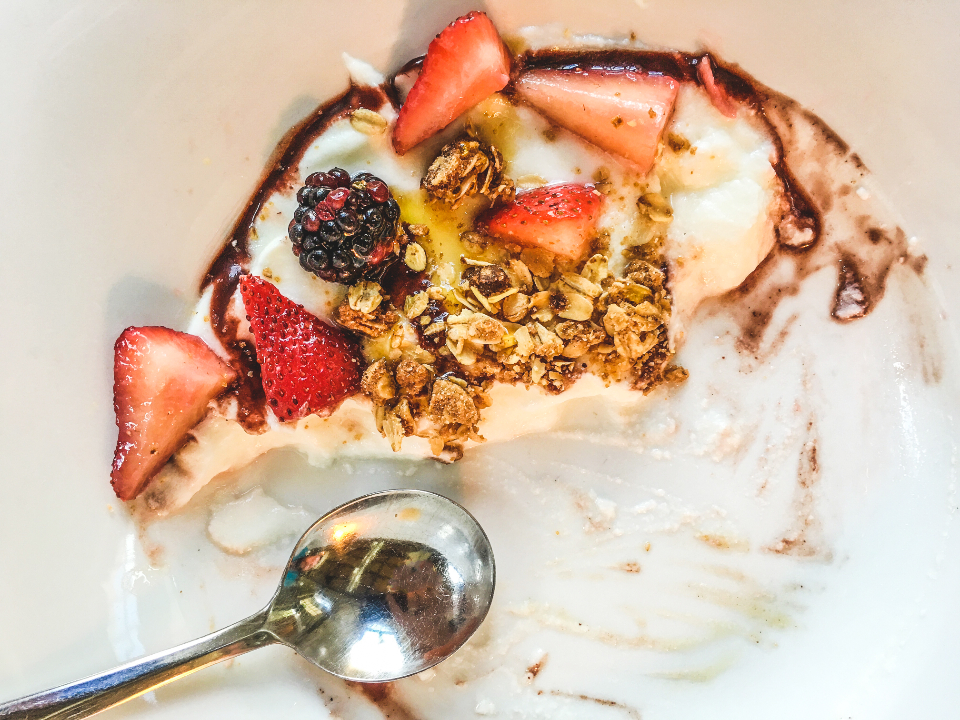 Yoghurt topped with sliced strawberries, berries and granola, with a spoon resting in the bowl