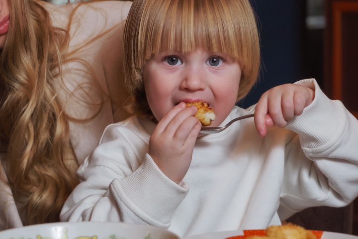 A young child eating a plate of dinner at the table at home